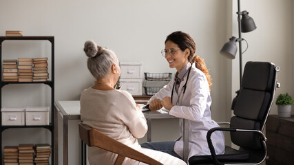 Wall Mural - You are doing well. Happy latin woman medic glad to inform senior female patient about positive treatment dynamics. Optimistic doc encourage elderly lady visitor tell good news about her health status