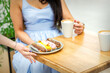© okskukuruza - Hand of waiter puts a plate with eclairs on the wooden table for young woman drinking coffee in a cafe