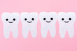 A row of white teeth with cartoon smiling faces, carved out of felt. Pink background. Copy space. The concept of stomatology and oral hygiene