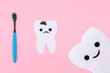 A smiling tooth cut out of the felt. In the background, in a blur, a sad tooth with caries and a toothbrush. Pink background. The concept of dental care and hygiene