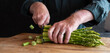 Hands cutting green asparagus on a wooden cutting board. Vegetables for a healthy eating concept. Gastronomy and lifestyle background. Close-up.