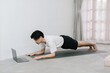 © Gengwit - Training At Home. Sporty man doing yoga while watching online tutorial on laptop, exercising in living room, free space