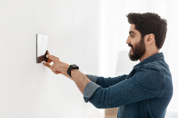 Poster - Bearded man controlling house with digital touch screen panel installed on light wall in the living room