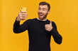 © timtimphoto - Bearded excited, happy looking man with brunette hair. Has piercing. Wearing black sweater. Making selfie and showing thumb up sign, approving gesture. Stand isolated over yellow background