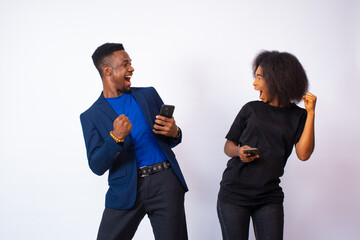 young black man and woman holding their phones next to each other rejoice about something