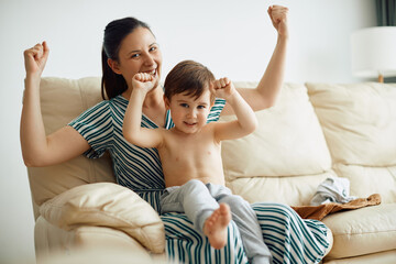 Wall Mural - Cute boy having fun with his mother and flexing muscles while dressing up at home.