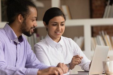 Canvas Print - Close up smiling Indian businesswoman mentor training African American intern, pointing finger at screen, helping with corporate software, giving instructions, diverse colleagues working together