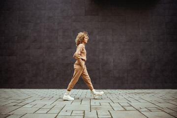 side view of trap girl in tracksuit walking with hands in her pockets and listening music.