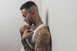 Portrait of a young handsome tattooed Spanish male posing leaning on a white wall