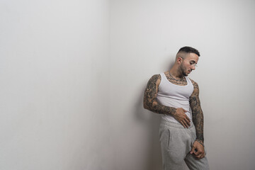 Wall Mural - Portrait of a young handsome tattooed Spanish male posing leaning on a white wall