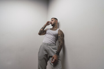 Canvas Print - Portrait of a young handsome tattooed Spanish male posing leaning on a white wall