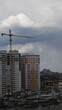 Construction site of unfinished multistory building with crane jib at overcast sky background. Under construction cityscape with rooftops and cloudscape. Vertical shot