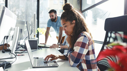 Young female programmer sitting at the desk in her office and working .	
