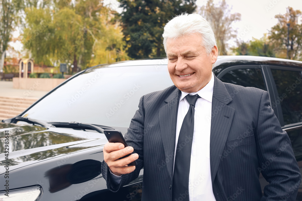 Senior businessman with mobile phone near modern car