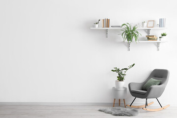 Shelves with books hanging on light wall and rocking chair in room