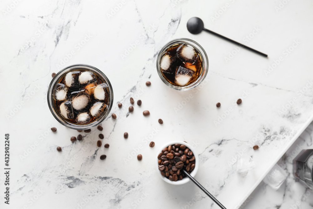 Glasses of tasty cold brew and coffee beans on light background