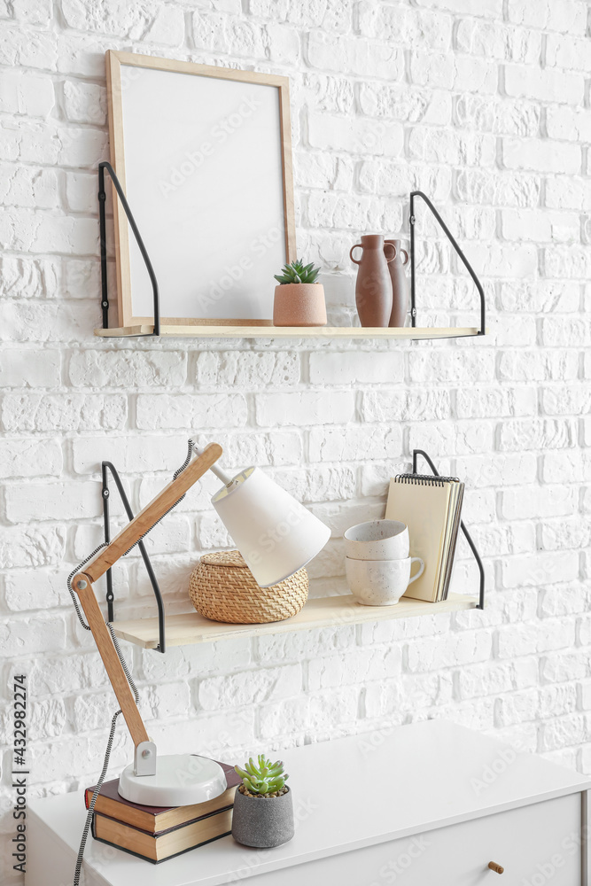 Modern shelves with decor and lamp near brick wall