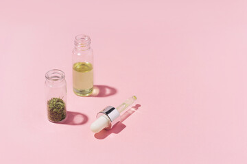 Two jars with dry cannabis and oil on pastel pink background