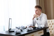© Alla - Frustrated young businessman is sitting at a table in front of a laptop. There is some crumpled paper on the table. Financial crisis concept. Photo in the interior. Copy space.