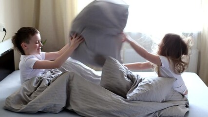 Wall Mural - Smiling little kids fight pillows on the bed in the morning. Happy sister and brother taking fun at home. slow motion