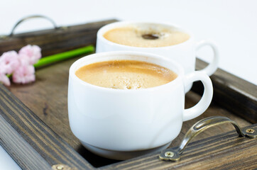 Two cups of frothy coffee. On a wooden tray. Hyacinth flowers. On white background.