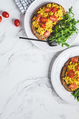 Wall Mural - Tofu scrambled toast with tomatoes and arugula on white plate, white marble background. Vegan food concept.