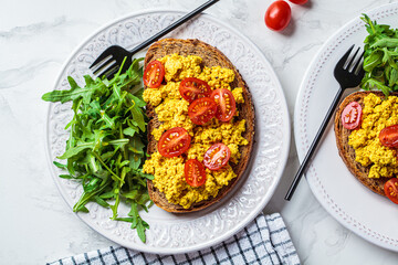 Wall Mural - Tofu scrambled toast with tomatoes and arugula on white plate, white marble background. Vegan food concept.