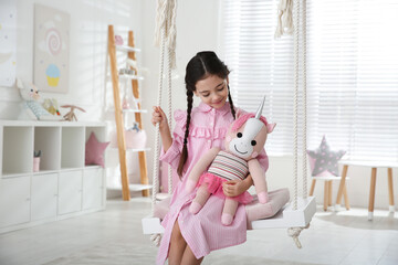 Canvas Print - Cute little girl playing with toy unicorn on swing at home