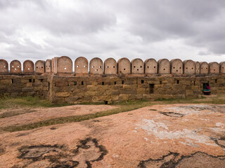 Poster - The stone ramparts and walls of the ancient Thirumayam Fort on a rocky hill with an overcast sky.