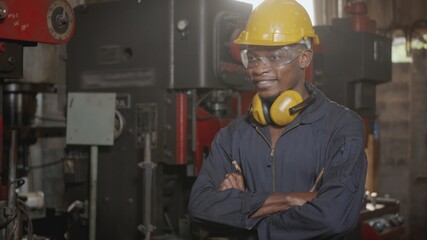 Portrait American industrial black young worker man smiling with yellow helmet in front of machine, Happy engineer standing arms crossed at work in the industry factory, manufacturing.