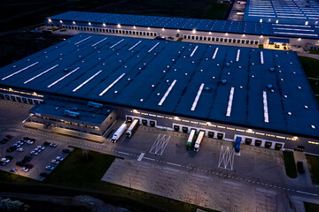 Sticker - Aerial view of goods warehouse at Night. Logistics center in industrial city zone from above. Aerial view of trucks loading at logistic center. View from drone.