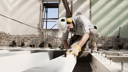 Wall Mural - man at work, construction worker wears helmet and uses the spirit level, check the beams at the base of the foundations of the second floor of house, in renovation building site background