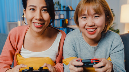 Canvas Print - Lesbian LGBTQ women couple play video game at home. Young Asia lady using wireless controller having funny happy moment on sofa in living room at night. They have great and fun time celebrate holiday.