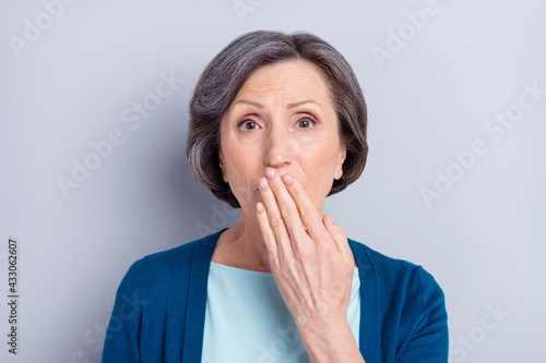 Photo portrait of elder woman shut mouth with hand keeping secret isolated on grey color background