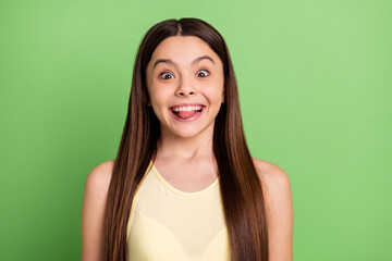 Poster - Photo of positive crazy pupil toothy smile biting tongue look camera isolated on green color background