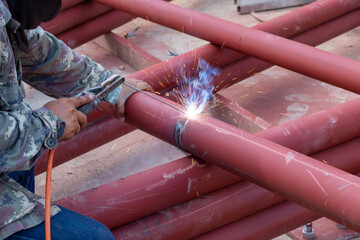 Wall Mural - A large red iron pole Being welded by a welder On the construction site The iron was painted with red rust-proof paint.