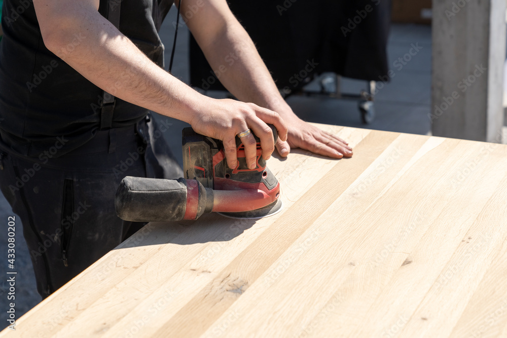 construction worker using a cordless power sander to sand a massive wooden table top - obrazy, fototapety, plakaty 