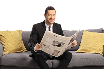 Wall Mural - Young businessman reading a newspaper ona sofa and smiling at the camera