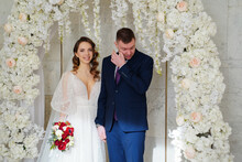 Bride And Groom In Arch Of Flowers At Wedding Ceremony. Man Cries With Happiness