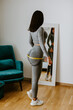 © shevtsovy - Fitness Woman Measuring butt With Tape at home. strong buttocks concept. Beautiful woman checking success of weight loss program and measuring butt and hips in front of mirror in living room.