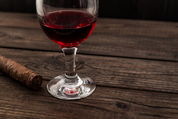 Glass of red wine and cuban cigar on an old wooden table. Angle view