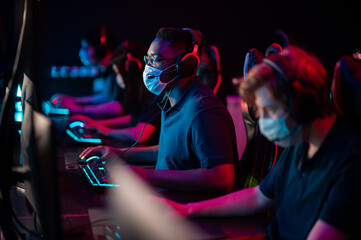 Wall Mural - White-skinned and black-skinned guys are members of an esports online strategy crew. Play at the computer at an international tournament during the pandemic.