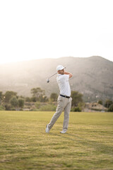 Golf player making a perfect swing on the golf course in the sunset.