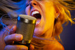 Female vocalist under gelled lighting sings with passion into condenser microphone.