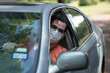 Young Man Wearing Medical Mask Looking Out Car Window With Inspection Car Tags on Windshield