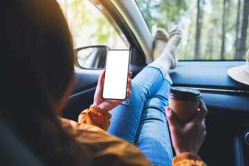 Mockup image of a woman holding and using mobile phone with blank screen while drinking coffee and laying in the car