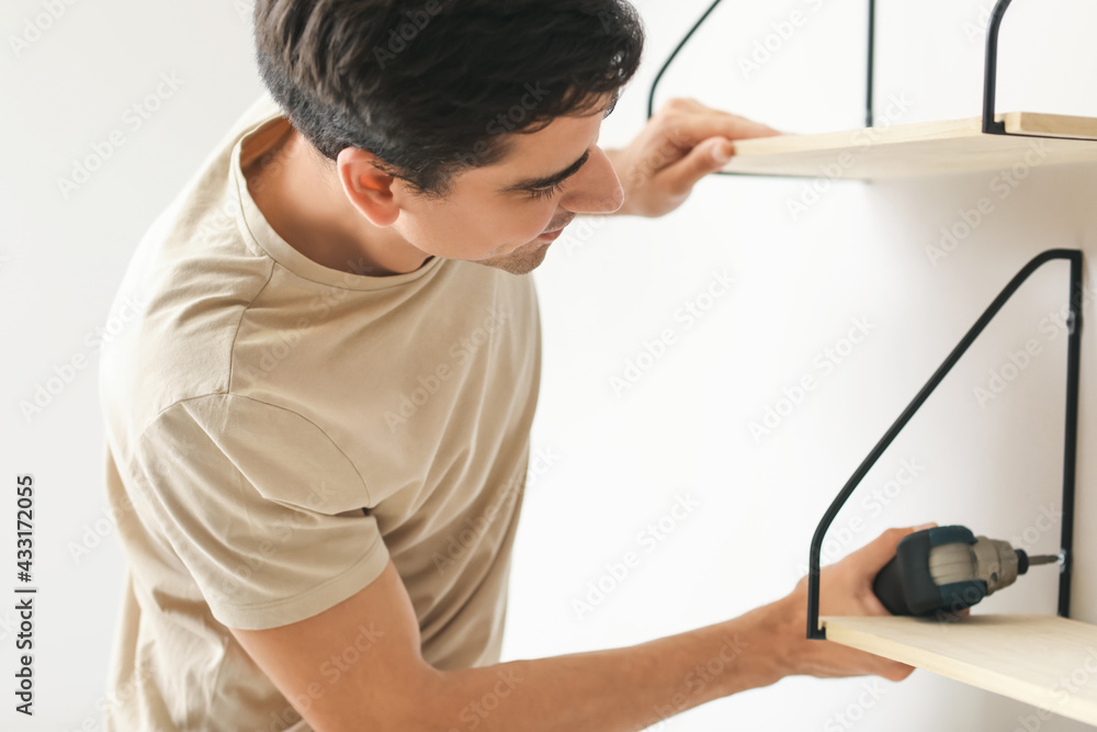 Young man installing modern shelves in room
