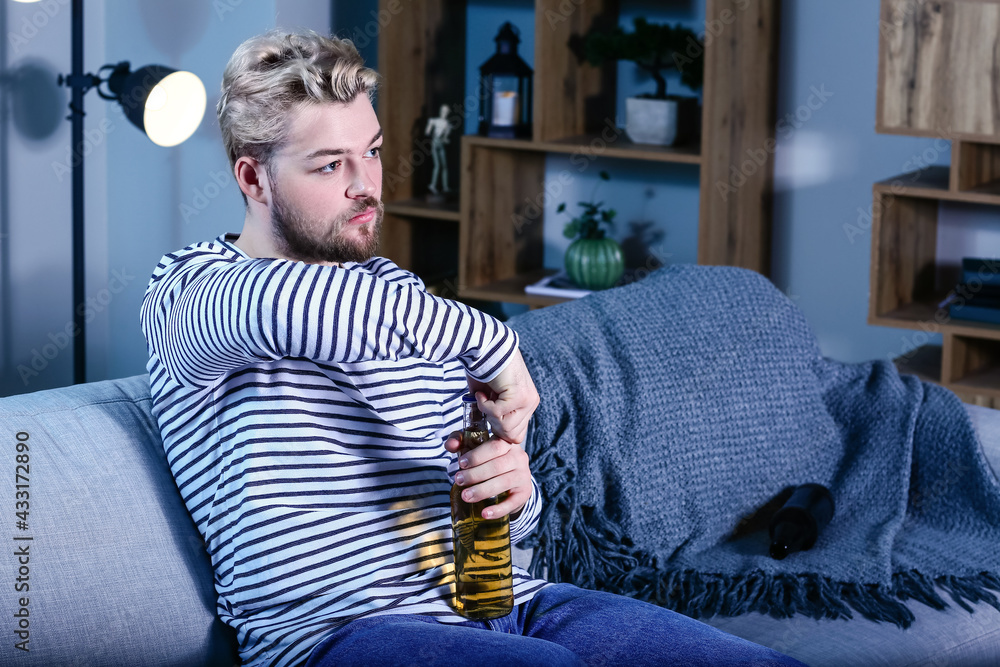 Young man drinking beer while watching TV at night. Concept of addiction