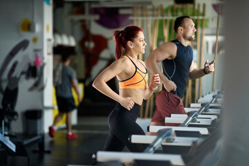 Wall Mural - Athletic couple running on treadmills while working out in a gym.