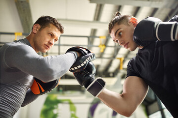 Wall Mural - Below view of young fighter exercising with a coach during sports training at the gym.